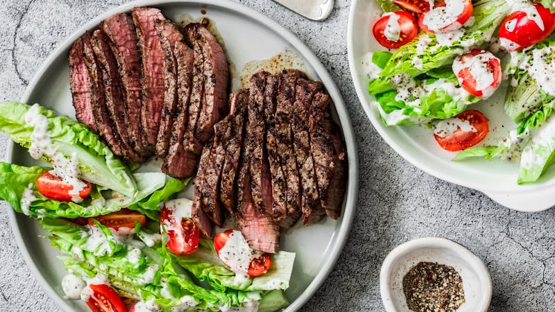 Beef medium rare steak and romaine salad cherry tomatoes yogurt dressing salad on a gray background, top view