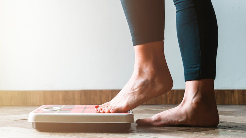 Female checking kilogrammes getting on the scale – self care and body positivity concept – warm flare on left